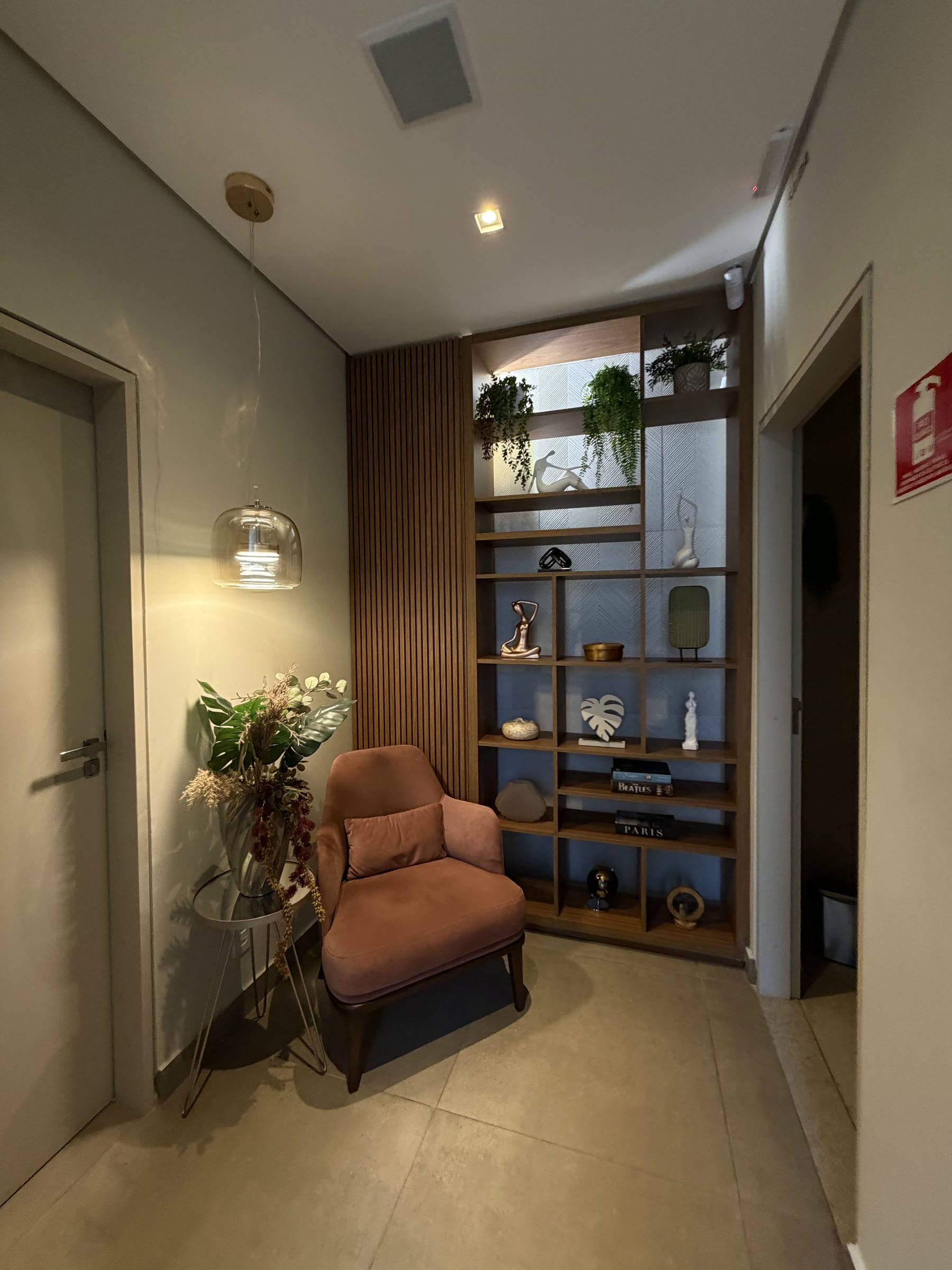 Recepção do consultório, com poltrona, estante decorada e arranjo de flores