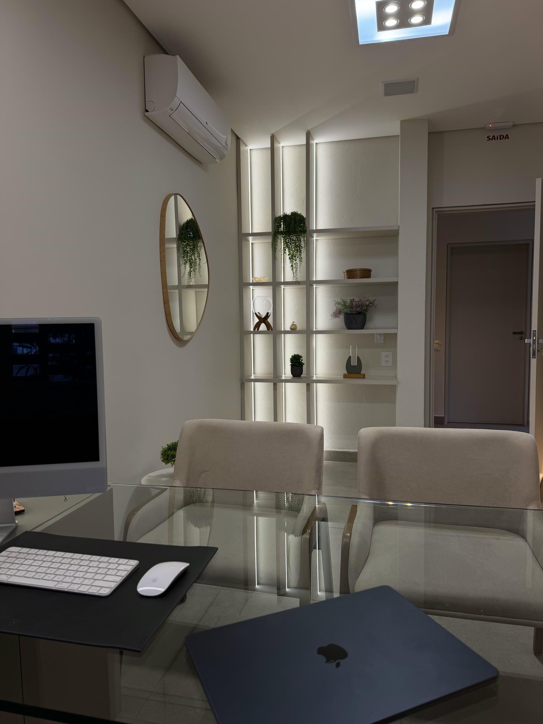 Mesa de atendimento com computador, diante de uma estante iluminada