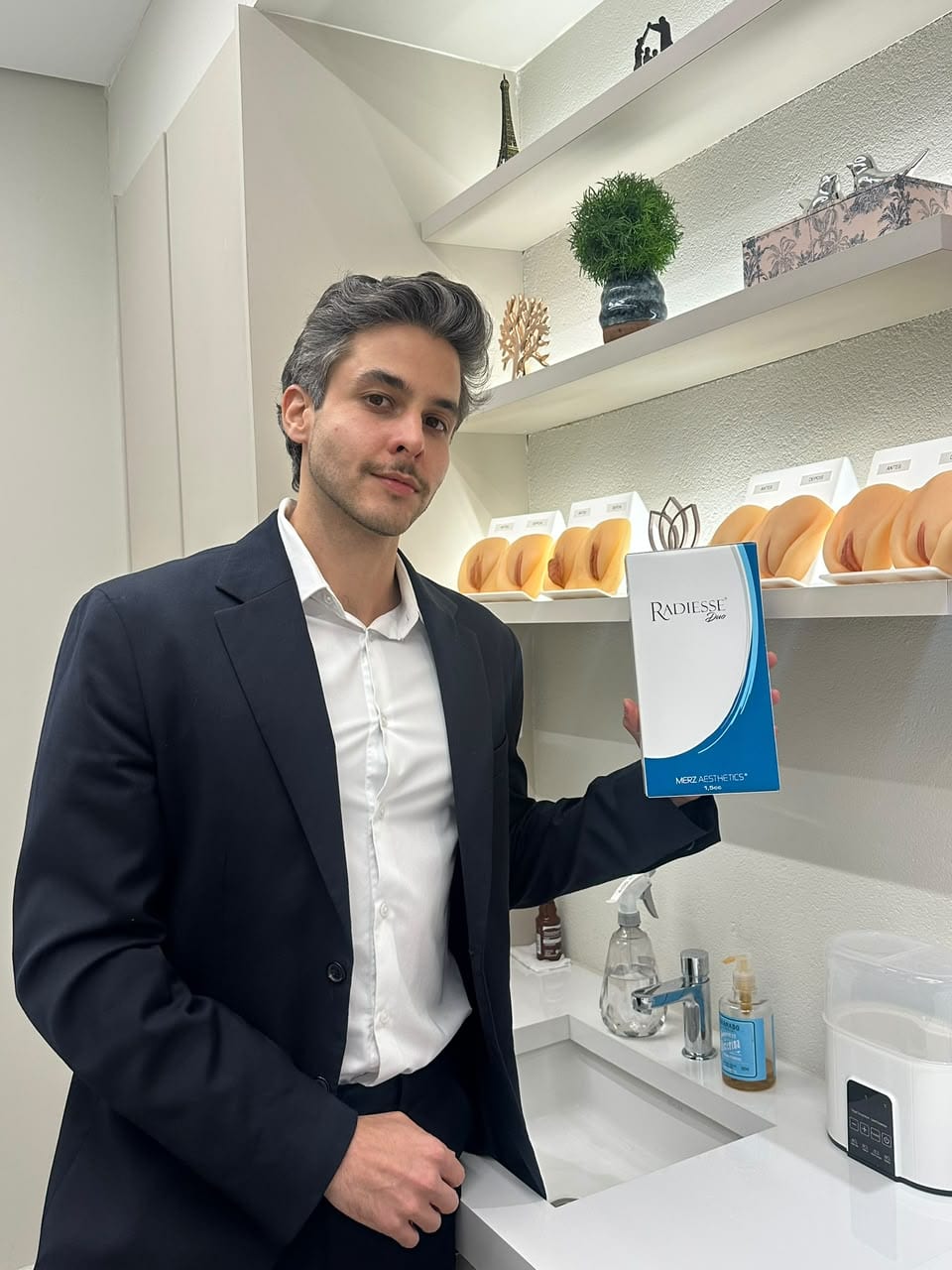 Dr. Milton Melo no consultório, segurando uma embalagem do bioestimulador de colágeno Radiesse